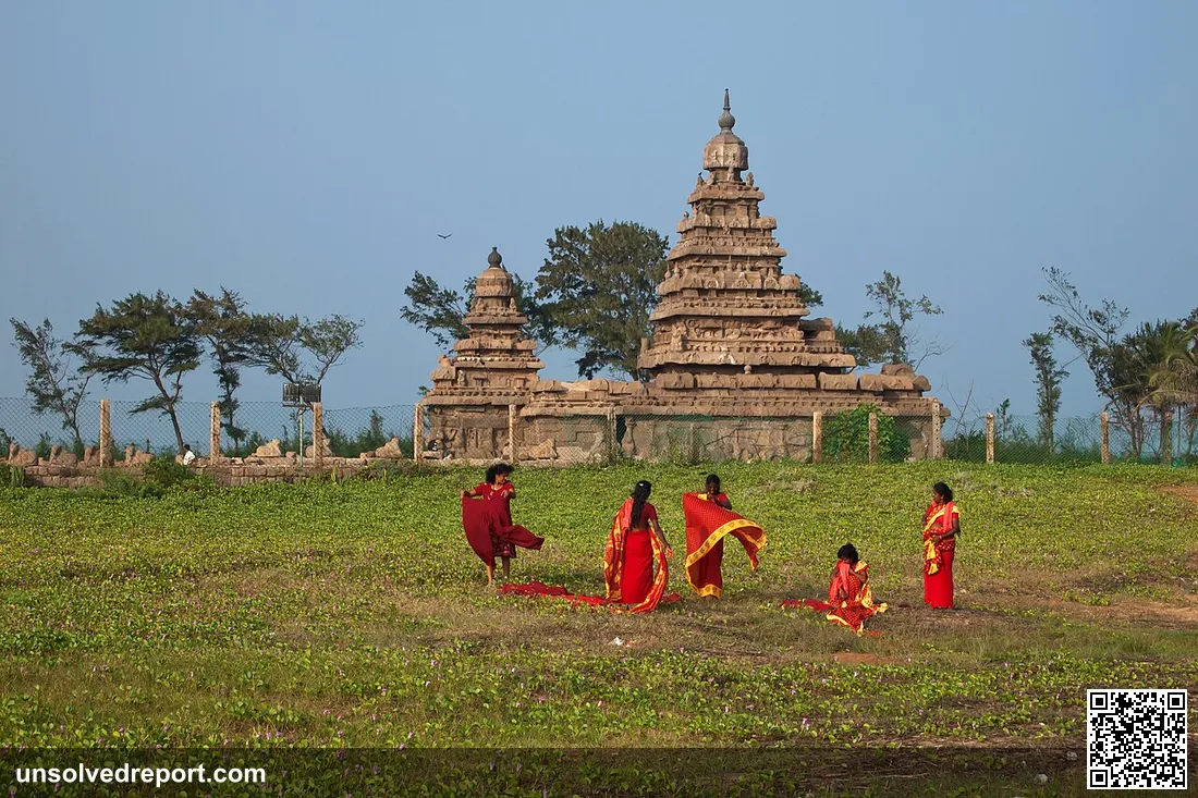 Five women wearing red and gold traditional Indian clothing (four in saris and one in a salwar-kameez) in front of the …