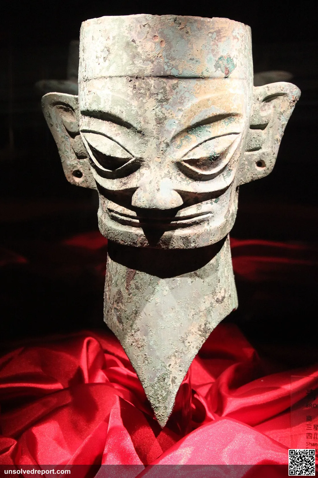 A Sanxingdui bronze head with sharp features and black paint outlining the eyes, on display at the Sanxingdui Museum.